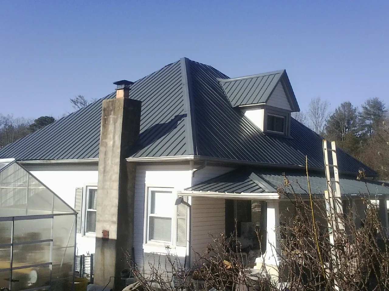 Dark blue standing seam metal roof on a white farmhouse with dormer — Slate & Tile Roof Repair by Roofing Brothers in Denhoff