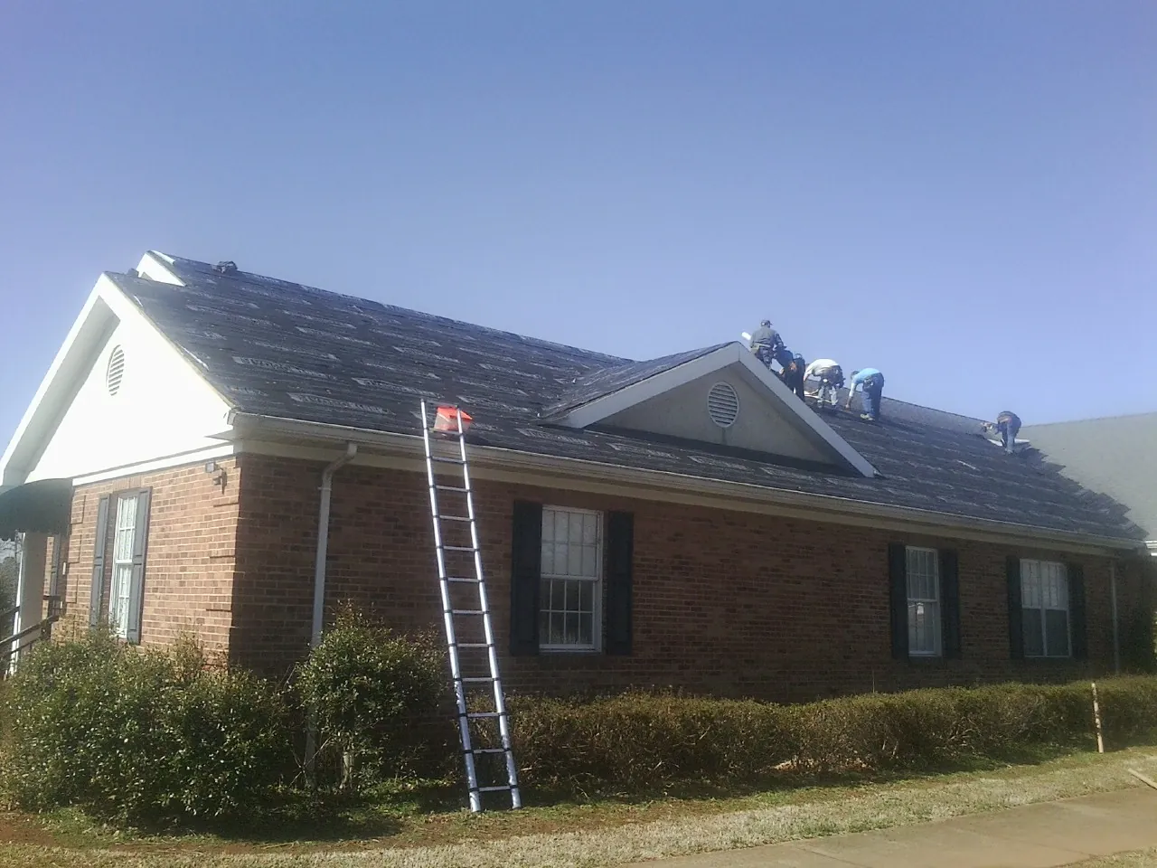 Crew tearing shingles off a brick ranch roof with a ladder set — Emergency Roof Repair work by our crew in Denhoff