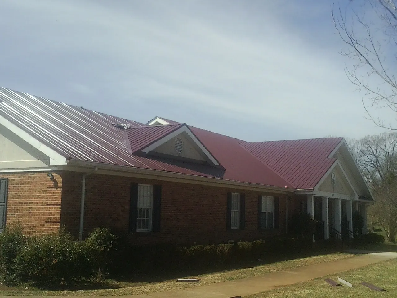 Red metal roof with gabled entries on a long brick building, from a Hail Damage Roof Repair job in Denhoff