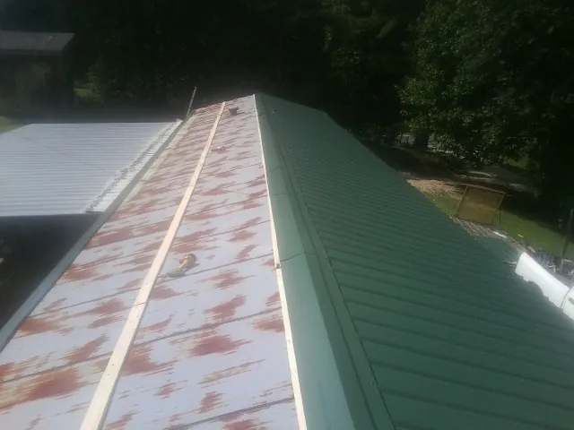 Old rusted panels beside newly installed green metal roofing — Wind Damage Roof Repair by Roofing Brothers in Denhoff